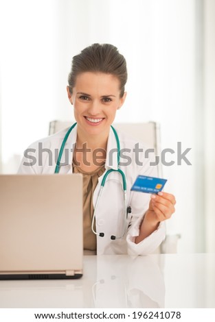 Portrait of happy medical doctor woman with credit card and laptop