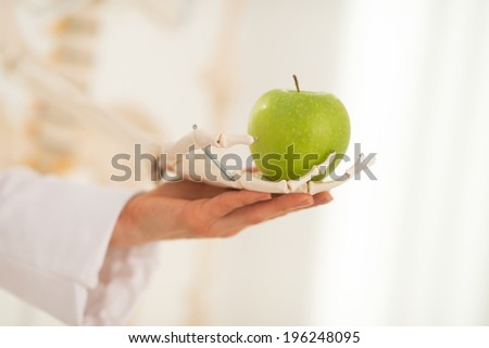 Closeup on medical doctor woman with human skeleton hand holding apple
