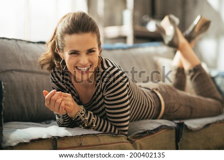 Portrait of smiling young woman laying on divan in loft apartment