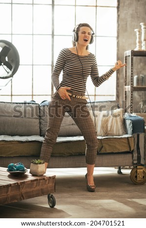 Full length portrait of young woman listening rock music in headphones in loft apartment