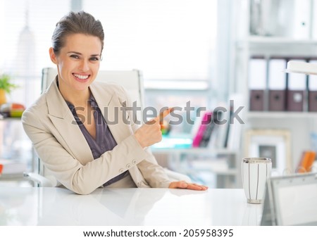 Happy business woman in office pointing on copy space
