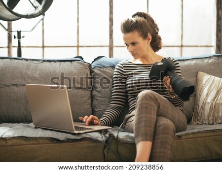Young woman with modern dslr photo camera using laptop in loft apartment