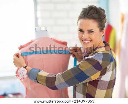 Portrait of happy tailor woman working with dress in studio