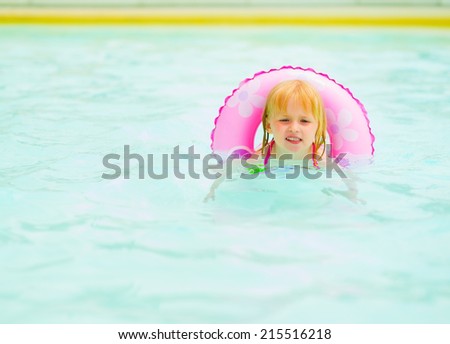 Baby girl with swim ring swimming in pool