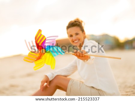 Closeup on young woman showing colorful windmill toy while sitting on the beach in the evening