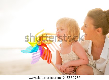 Mother and baby girl playing with colorful windmill toy on the beach in the evening