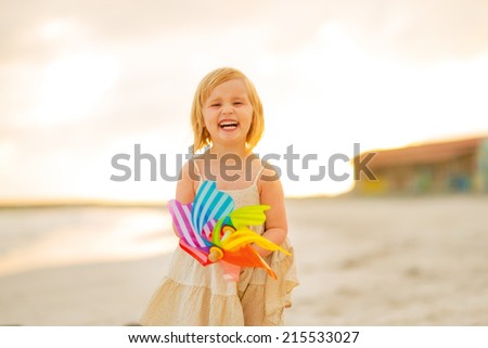 Portrait of smiling baby girl with colorful windmill toy on the beach in the evening
