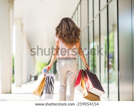 Young woman with shopping bags walking on the mall alley. rear view