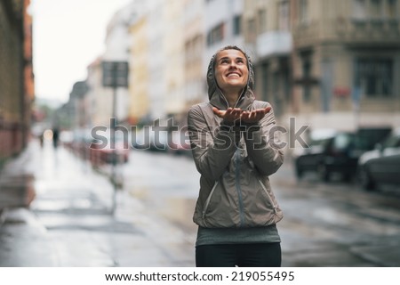 Happy fitness young woman catching rain drops in the city