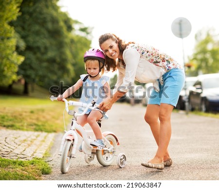 Mother helping baby girl riding bicycle