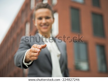 Closeup on happy business woman stretching hand for handshake in front of office building
