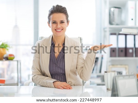 Happy business woman presenting something on empty palm in office