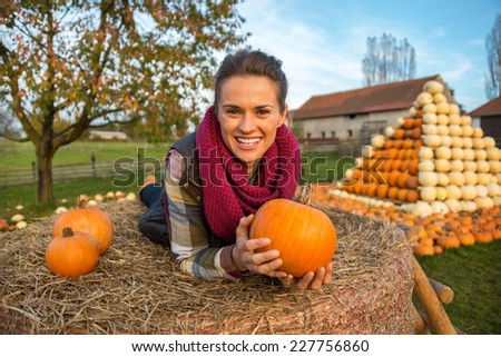 Portrait of smiling young woman laying on haystack with pumpkins in front of pumpkin piramide