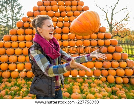 Happy young woman throwing pumpkin in front of pumpkin rows