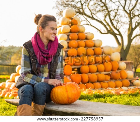 Portrait of happy young woman sitting with pumpkin in front of pumpkin piramide