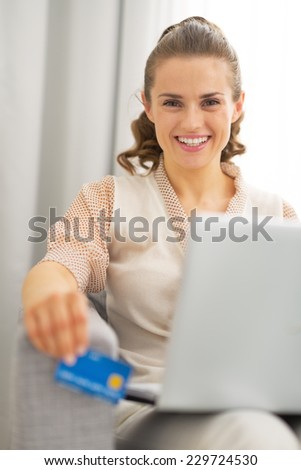 Portrait of happy young housewife with laptop holding credit card