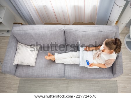 Young housewife laying on sofa in living room and making online shopping