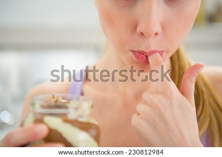 Closeup on young woman licking chocolate butter from finger
