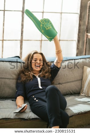 Portrait of happy football fan woman watching tv in loft apartment