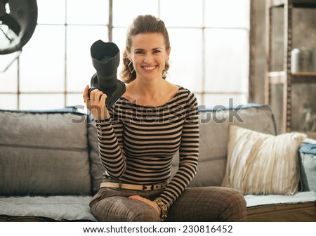 Portrait of smiling young woman with dslr photo camera sitting in loft apartment