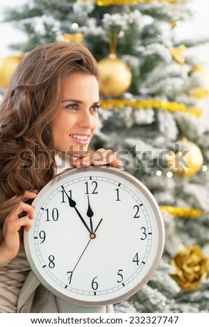 Profile portrait of smiling young woman with clock near christmas tree