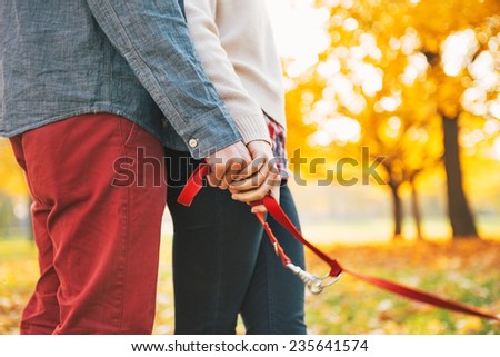 Closeup on young couple holding leash together in autumn park