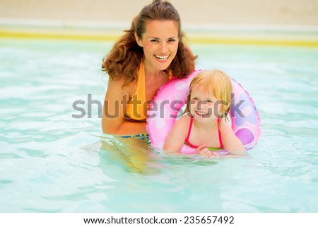 Portrait of happy mother and baby girl with swim ring swimming in pool