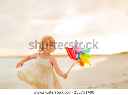 Baby girl playing with colorful windmill toy on beach