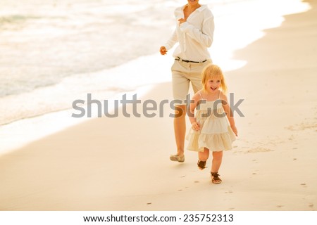 Mother and baby girl running on beach at the evening