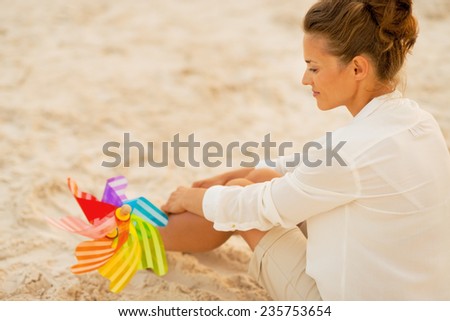 Young woman with colorful windmill toy sitting on beach at the evening. rear view