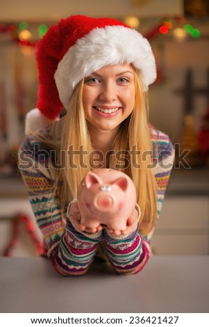 Smiling teenager girl in santa hat showing piggy bank