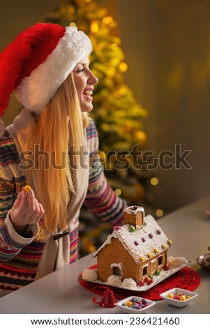 Happy teenager girl in santa hat decorating christmas cookie house