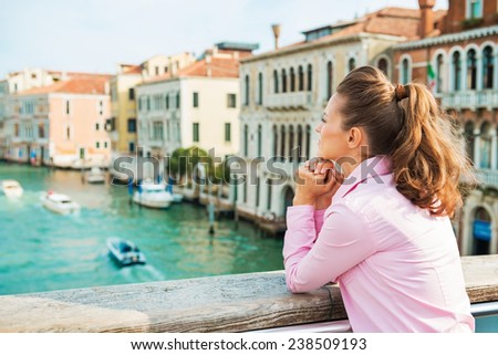 Happy young woman standing on bridge with grand canal view in venice, italy and looking into distance