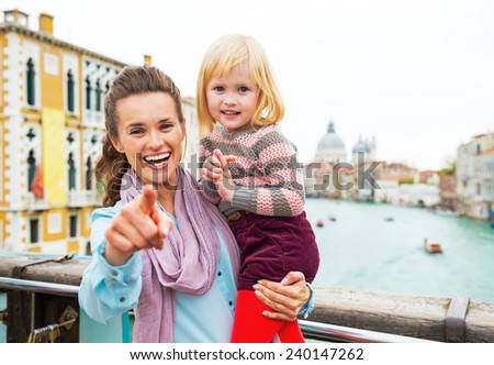 Baby girl and mother poiting in camera while standing on bridge with grand canal view in venice, italy