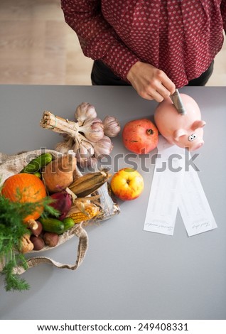 Closeup on young housewife putting money into piggy bank after shopping on local market