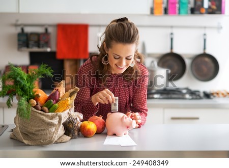 Portrait of happy young housewife putting money into piggy bank after shopping on local market