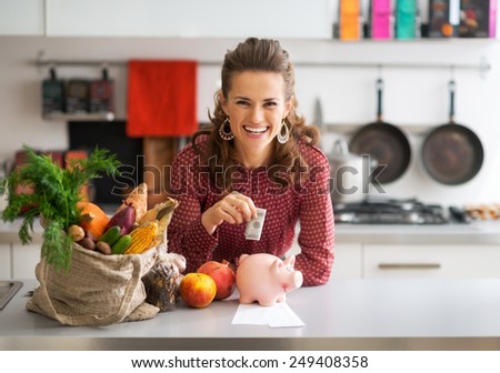 Portrait of happy young housewife putting money into piggy bank after shopping on local market