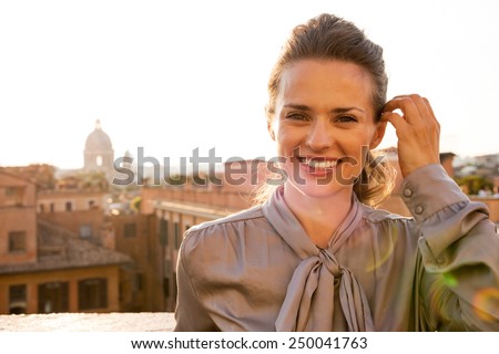 Portrait of happy young woman standing on street overlooking rooftops of rome on sunset