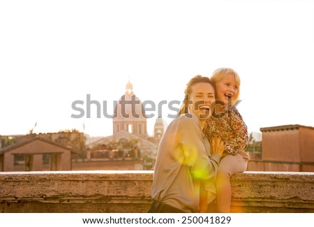 Portrait of smiling mother and baby girl on street overlooking rooftops of rome on sunset