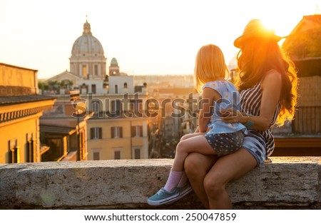 Mother and baby girl sitting on street overlooking rooftops of rome on sunset looking into distance