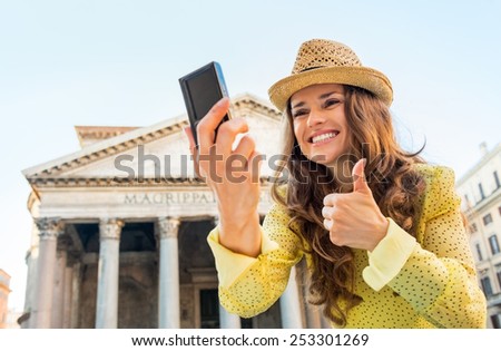 Portrait of happy young woman making selfie and showing thumbs up in front of pantheon in rome, italy