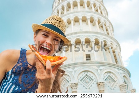 Happy young woman eating pizza in front of leaning tower of pisa, tuscany, italy