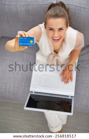 Happy young woman with laptop showing credit card