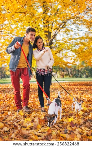 Happy young couple walking outdoors in autumn park with dogs
