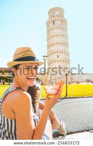 Portrait of happy young woman eating pizza in front of leaning tower of pisa, tuscany, italy