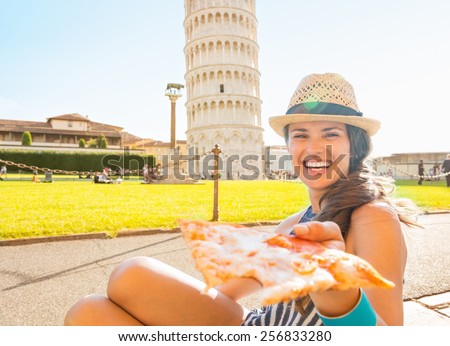 Young woman giving pizza in front of leaning tower of pisa, tuscany, italy