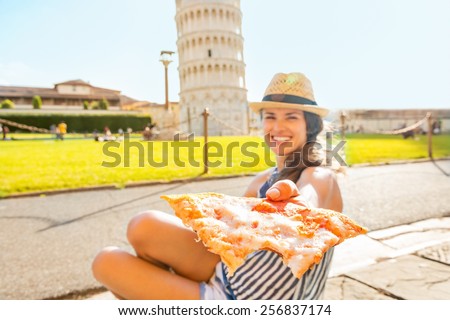 Closeup on young woman giving pizza in front of leaning tower of pisa, tuscany, italy