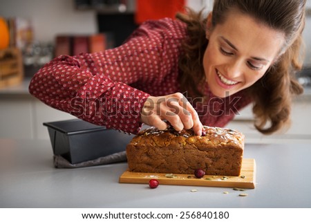 Closeup on happy young housewife decorating freshly baked pumpkin bread with seeds