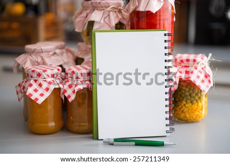 Closeup on notepad among jars with homemade fruits jam and pickled vegetables