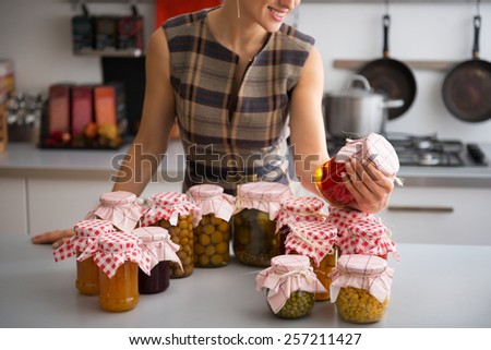 Closeup on young housewife checking jars with homemade fruits jam and pickled vegetables